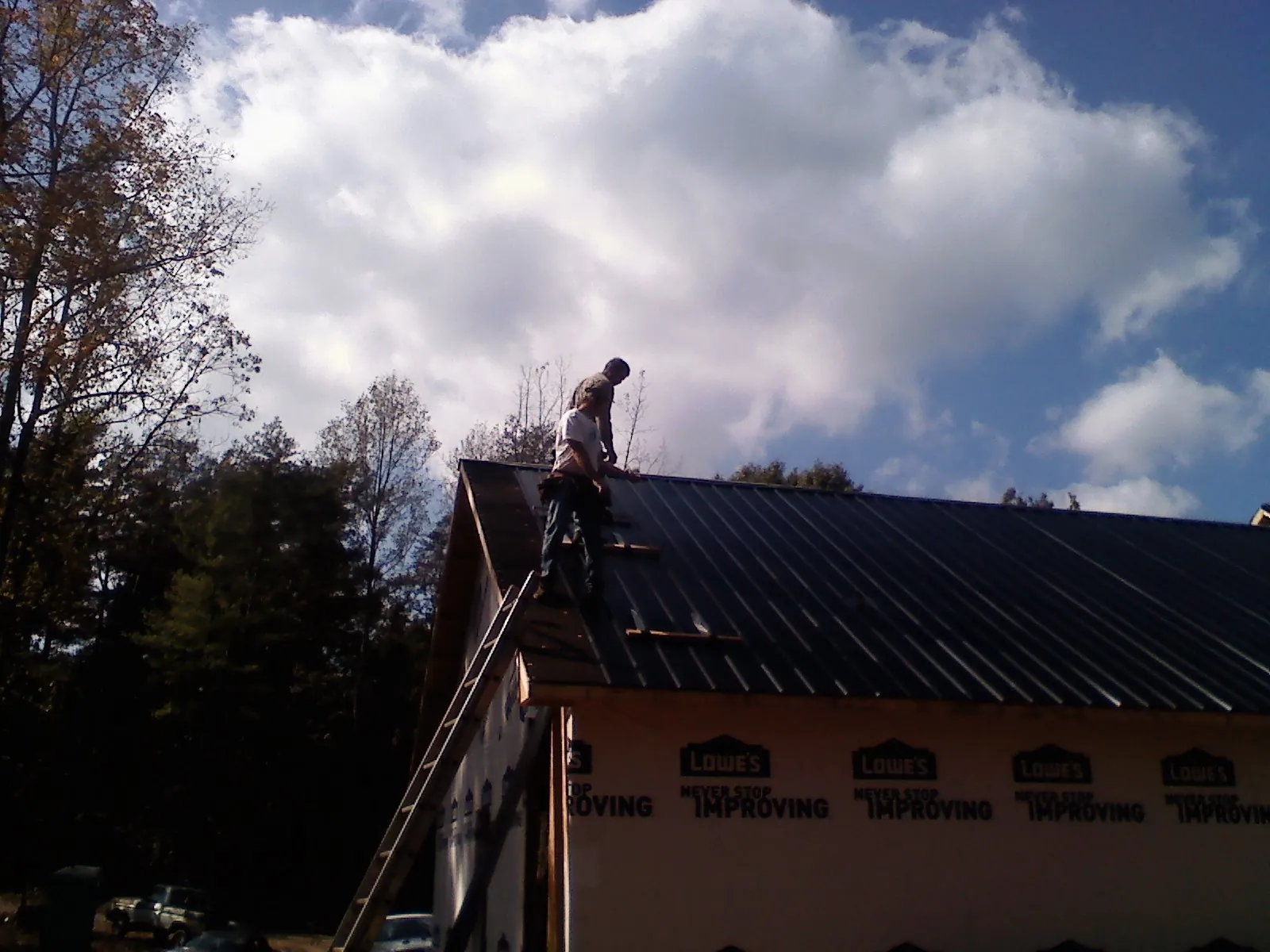 Roofer fastening dark metal panels high against a cloudy sky, from a Roof Inspection job in Bowersville