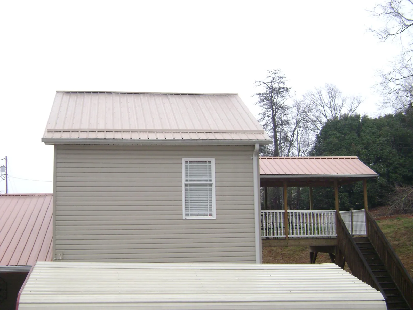 Tan metal roofs on a two story addition and attached porch, from a Roof Replacement job in Bowersville